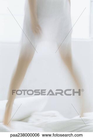 Stock Photograph - Woman standing on bed, low section, blurred. Fotosearch
