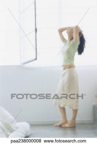 Stock Photo - Young woman standing with head back and hands on head, full length, blurred. Fotosearch