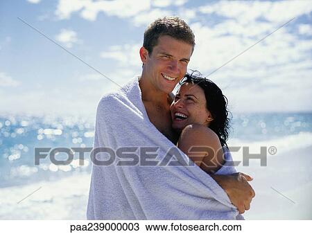 Stock Image - Couple hugging, sea in background, portrait. Fotosearch