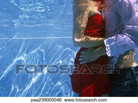 Stock Photograph - Couple in clothes embracing, mid-section, underwater view. Fotosearch