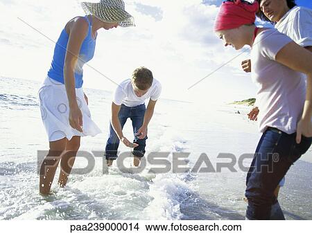 Picture - Four people standing in surf. Fotosearch