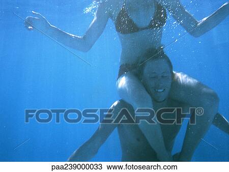 Stock Image - Man carrying woman on shoulders, underwater view. Fotosearch