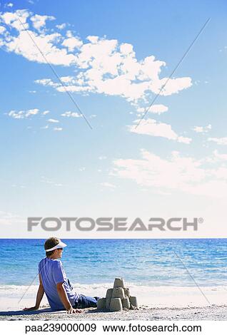 Man sitting near sand castle, looking out to sea View Large Photo Image Stock Photo - Man sitting near sand castle, looking out to sea. Fotosearch