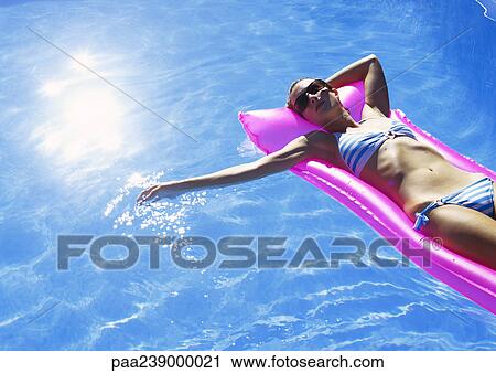 Stock Image - Woman lying on air mattress, elevated view. Fotosearch