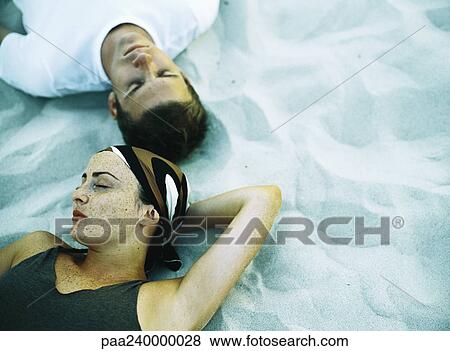 Couple lying on sand, eyes closed, elevated view View Large Photo Image Stock Photo - Couple lying on sand, eyes closed, elevated view. Fotosearch