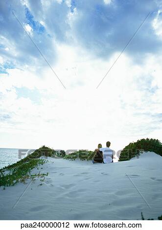 Couple on sand dune looking out to sea, rear view View Large Photo Image Stock Image - Couple on sand dune looking out to sea, rear view. Fotosearch
