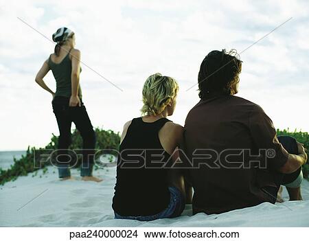 Couple sitting and woman standing on sand dune, rear view View Large Photo Image Picture - Couple sitting and woman standing on sand dune, rear view. Fotosearch