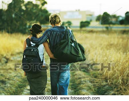Couple walking with arms around each other through field, rear view View Large Photo Image Stock Photograph - Couple walking with arms around each other through field, rear view. Fotosearch