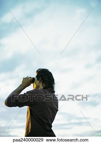 Stock Photo - Man looking through binoculars, low angle view. Fotosearch