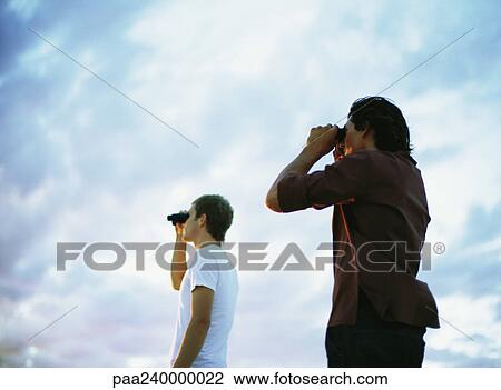 Two people looking through binoculars, low angle view View Large Photo Image Stock Image - Two people looking through binoculars, low angle view. Fotosearch
