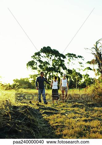 Two women and man walking in field View Large Photo Image Stock Image - Two women and man walking in field. Fotosearch