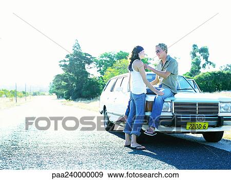 Stock Photo - Woman face to face with man sitting on car hood. Fotosearch