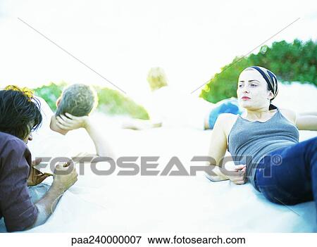 Stock Photo - Women and men lying on sand. Fotosearch