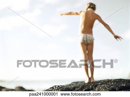 Stock Image - Child balancing on rock, rear view, blurred. Fotosearch