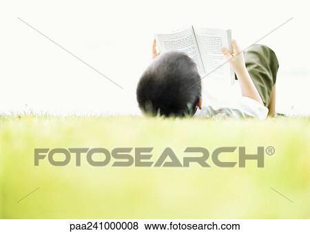 Child lying on back on grass, reading, rear view View Large Photo Image Stock Photo - Child lying on back on grass, reading, rear view. Fotosearch