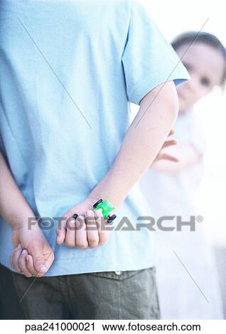 Stock Image - Child with hands behind back, one holding toy car, close-up, girl in background reaching. Fotosearch