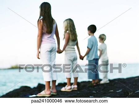 Stock Photograph - Children standing, holding hands, looking out to sea. Fotosearch