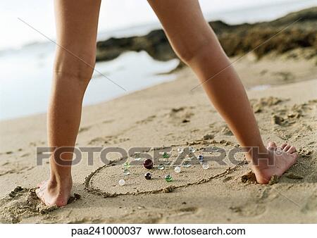 Stock Photo - Child's legs above marbles on sand, low section, close-up. Fotosearch