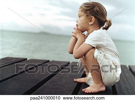 Girl crouching on dock, sea in background View Large Photo Image Stock Image - Girl crouching on dock, sea in background. Fotosearch