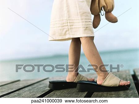 Stock Photo - Girl wearing woman's shoes, low section, sea in background. Fotosearch