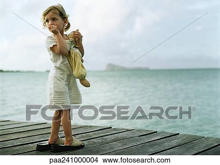 Picture - Little girl standing on dock, sucking thumb and looking over shoulder. Fotosearch