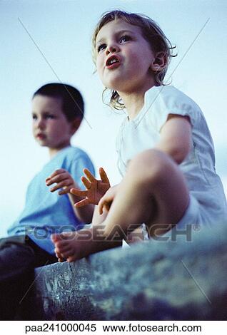 Two children sitting outdoors, low angle view View Large Photo Image Stock Photography - Two children sitting outdoors, low angle view. Fotosearch