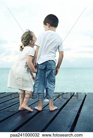 Two children standing on dock, rear view View Large Photo Image Stock Image - Two children standing on dock, rear view. Fotosearch