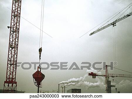 Stock Image - Cranes and factory smoke stacks, low angle view. Fotosearch