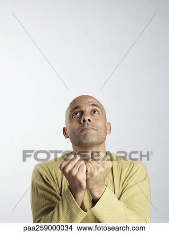 Picture - Young man looking up, holding fists togther in front of him. Fotosearch