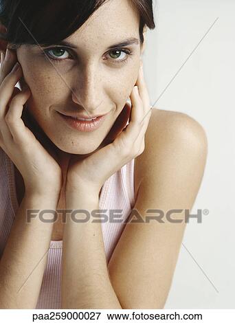 Stock Photo - Young woman holding face between hands, close-up. Fotosearch