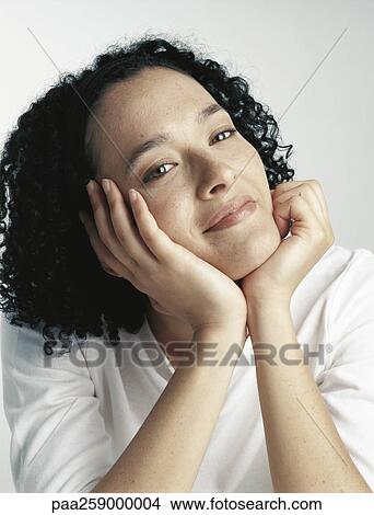 Picture - Young woman holding head with hands, looking at camera. Fotosearch