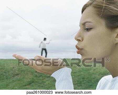 Woman in foreground holding out palm and blowing kiss, man in distant background, optical illusion View Large Photo Image Stock Image - Woman in foreground holding out palm and blowing kiss, man in distant background, optical illusion. Fotosearch