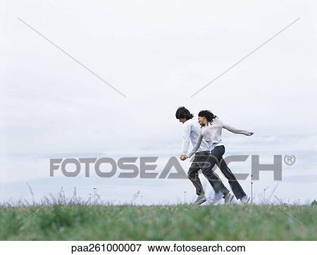 Stock Photo - Young man and woman holding hands and running on grass. Fotosearch