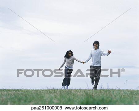 Stock Photo - Young man and woman holding hands and running on grass. Fotosearch
