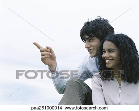 Picture - Young man and woman sitting together, young man pointing. Fotosearch