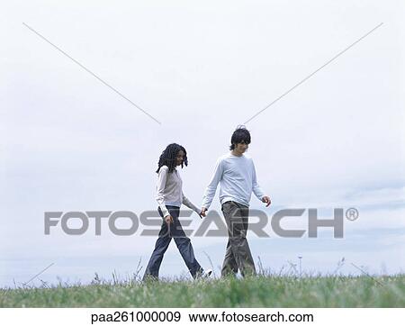 Stock Photo - Young man and woman walking on grass holding hands. Fotosearch