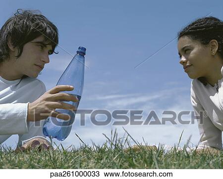 Young man and young woman leaning on elbows in grass, young man holding out bottle View Large Photo Image Stock Image - Young man and young woman leaning on elbows in grass, young man holding out bottle. Fotosearch