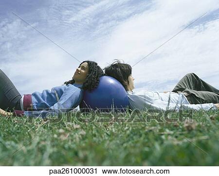Young man and young woman lying back to back in grass, leaning heads on ball View Large Photo Image Stock Image - Young man and young woman lying back to back in grass, leaning heads on ball. Fotosearch