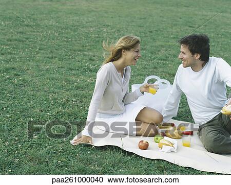 Young man and young woman sitting on blanket on grass having picnic View Large Photo Image Stock Image - Young man and young woman sitting on blanket on grass having picnic. Fotosearch
