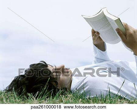 Young man lying on back in grass reading book, head and shoulders View Large Photo Image Stock Photo - Young man lying on back in grass reading book, head and shoulders. Fotosearch
