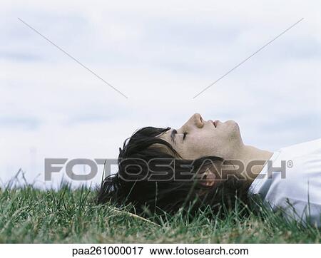 Young man lying on back in grass with eyes closed, head and shoulders View Large Photo Image Stock Photo - Young man lying on back in grass with eyes closed, head and shoulders. Fotosearch