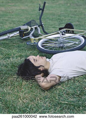 Young man lying on back on grass next to bicycle View Large Photo Image Stock Image - Young man lying on back on grass next to bicycle. Fotosearch