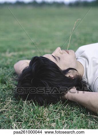 Young man lying on back with hands behind head and piece of grass in mouth View Large Photo Image Picture - Young man lying on back with hands behind head and piece of grass in mouth. Fotosearch