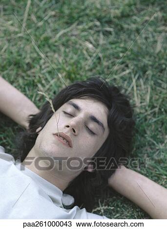 Young man lying on grass with eyes closed and piece of grass in mouth View Large Photo Image Stock Image - Young man lying on grass with eyes closed and piece of grass in mouth. Fotosearch