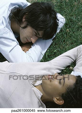 Stock Photography - Young man lying on stomach and young woman lying on back on grass, head and shoulders. Fotosearch