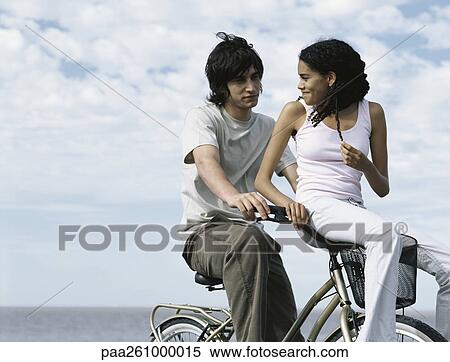 Young man sitting on bicycle, young woman sitting on bicycle basket looking over shoulder at young man View Large Photo Image Stock Photography - Young man sitting on bicycle, young woman sitting on bicycle basket looking over shoulder at young man. Fotosearch