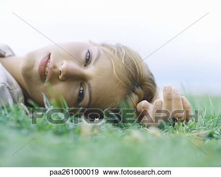 Young woman lying on back on grass with hand above head, head shot View Large Photo Image Stock Photo - Young woman lying on back on grass with hand above head, head shot. Fotosearch