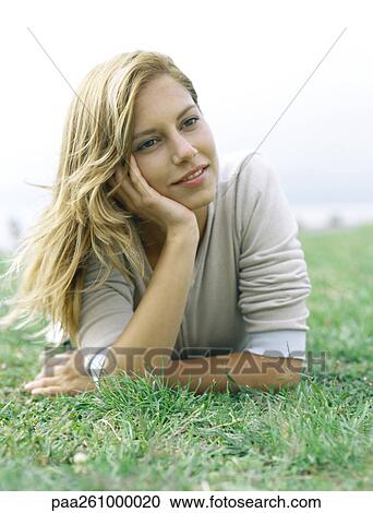 Young woman lying on stomach on grass, propping up head with hand View Large Photo Image Stock Image - Young woman lying on stomach on grass, propping up head with hand. Fotosearch