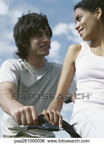 Young woman sitting on handlebars, looking over shoulder at young man View Large Photo Image Stock Photograph - Young woman sitting on handlebars, looking over shoulder at young man. Fotosearch