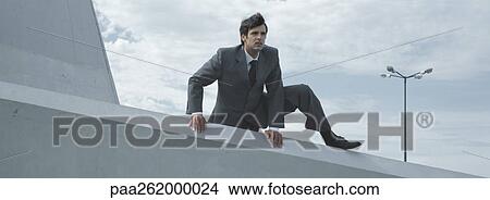 Picture - Man in suit climbing over low concrete wall. Fotosearch